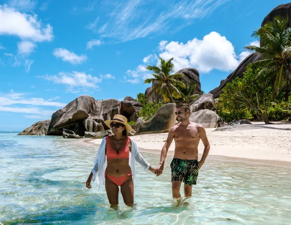 Neşeli bir çift, La Digue Seyşeller 'deki Anse Source d' Argent sahilinin sığ sularında el ele dolaşır..