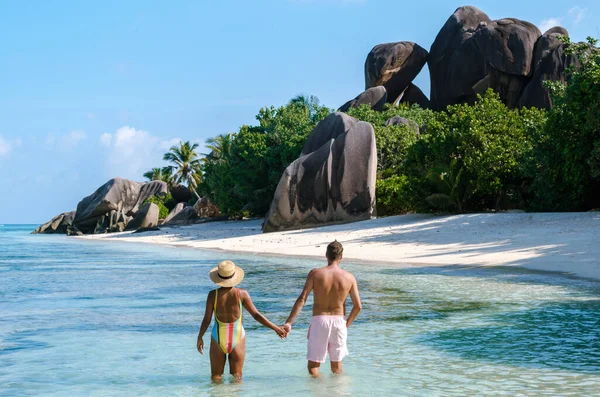 Bir çift, görkemli granit kayalar ve yemyeşil yeşilliklerle çevrili Anse Kaynak d 'Argent sahilinin sakin suları boyunca el ele yürür. La Digue, Seyşeller 'de güneşin altında mükemmel bir gün.