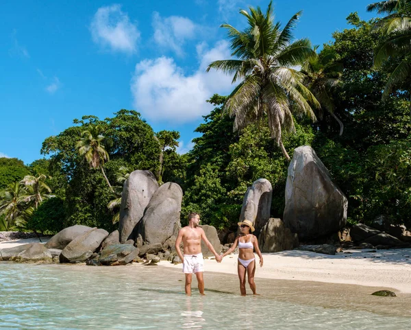 Bir çift, Anse Royale sahilinin altın kumlarında romantik bir yürüyüş yapar, Mahe, Seyşeller. Kristal berrak sular, bereketli palmiyeler ve engebeli kayalar tarafından çerçevelenmiş, yavaşça ayaklarının üzerinde döner.