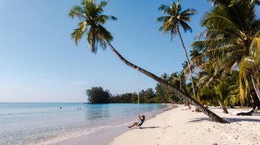 Khlong Hin Sahili 'nde, Koh Kood Tayland' da bir salıncakta sallanmaktan hoşlanan bir insan. Açık mavi su ve yumuşak beyaz kum mükemmel bir tropikal kaçış yaratır..