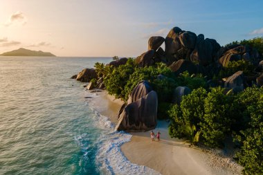 Altın güneş ışığı Anse Source d 'Argent plajını yıkıyor, yükselen granit kayaları aydınlatıyor. Çiftler sakin kıyı şeridinde gezerler, La Digue, Seyşeller 'de romantik bir atmosfer yaratırlar.