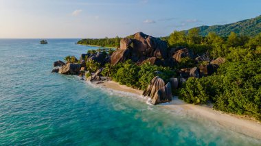 Dalgalar yumuşak kumlu kıyıya hafifçe vururken yemyeşil ve ikonik granit kayalar Anse Source d 'Argent plajı, La Digue, Seychelles
