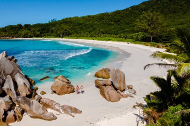 Yumuşak beyaz kumlar ve turkuaz sular La Digue 'deki Anse Cocos plajında sakin bir kaçış sağlar. Kumsalda yürüyen bir çift erkek ve kadın, İHA hava manzaralı Seyşeller
