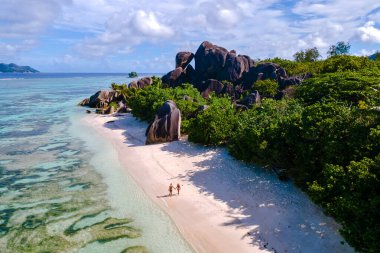 Kristal berrak sular ve eşsiz granit kayalar Anse Source d 'Argent plajında pitoresk bir manzara yaratır. Çift, yumuşak kumda geziniyor, La Digue Seyşeller 'in dingin güzelliğinin tadını çıkarıyor..