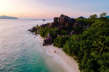 Kıyıya vuran yumuşak dalgalar, parlak kayalar ve yemyeşil çimenlik Anse Kaynak d 'Argent sahilinin el değmemiş kumları. Gün batımında sahilde bir çift, La Digue, Seyşeller