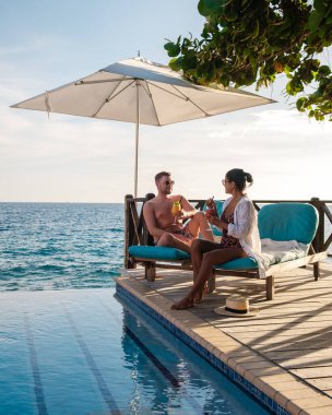 Çeşitli bir çift, Willemstad 'daki köpüklü okyanusun kıyısındaki güvertede uzanırken ferahlatıcı içeceklerin tadını çıkarıyor. Curacao 'da tatilde olan bir adam ve bir kadın havuzda dinleniyorlar.