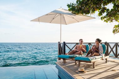 Çeşitli erkek ve kadınlar Curacao 'da okyanusun kenarında uzanırken kokteyl içmekten zevk alırlar. Güneş, huzur dolu sonsuz havuzun üzerinde ışıl ışıl parlıyor. Bu da onu rahatlamak için ideal bir yer yapıyor.