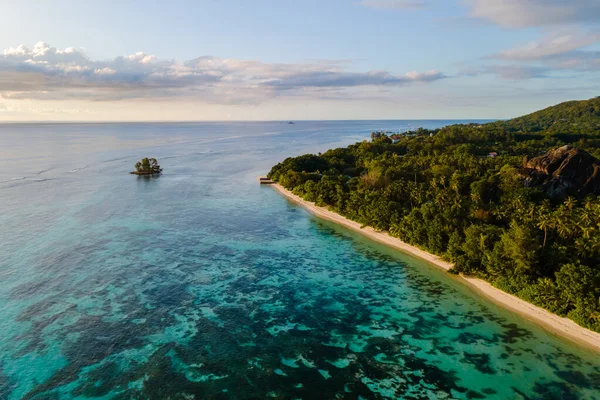Güneş batarken dalgalar yavaşça Anse Source d 'Argent sahillerini kaplıyor, dingin manzaranın üzerine sıcak renkler döküyor. Tropik esintide sallanan palmiyeler, La Digue, Seyşeller