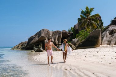 Anse Source d 'Argent, La Digue, Seyşeller, bir çift, yumuşak beyaz kumda keyifli bir yürüyüş yapar. Berrak turkuaz sular ve görkemli granit kayalar tropik bir cennet yaratır..