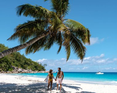 Praslin Seyşeller 'deki Anse Georgette sahilinin el ele tutuşmuş kumları boyunca el ele dolaşırlar..
