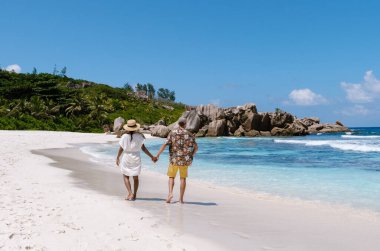 White sands stretch along Anse Cocos beach, where a couple walks hand in hand under the sun. La Digue Seychelles