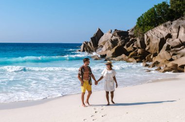 Çift, La Digue, Seyşeller 'deki Anse Cocos plajında romantik bir yürüyüşün tadını çıkarıyor. Turkuaz sular nazikçe ayaklarının altında dolaşarak cennette huzurlu bir tatil atmosferi yaratıyor..