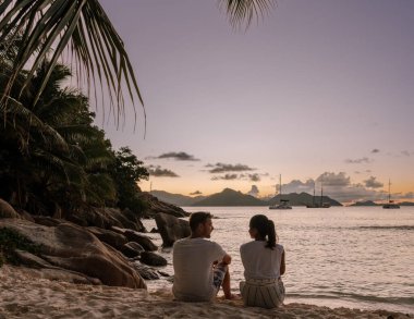 Anse Patates, La Digue, Seyşeller 'in huzurlu ortamında bir çift yumuşak kumda oturur ve büyüleyici günbatımını seyrederler..
