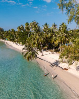 Ziyaretçiler Koh Kood, Tayland 'daki Khlong Hin Sahili' nin sakinliğinin tadını çıkarıyorlar. Güneş yumuşak kum ve turkuaz suyun üzerinde ışıl ışıl parlıyor, rüzgarda hafifçe sallanan gür palmiyelerle çevrili..