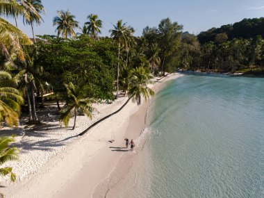 İki sahil sakini Koh Kood, Tayland 'daki Khlong Hin Sahili' nin yumuşak kumlarında sakin bir yürüyüşün tadını çıkarıyorlar. Uzun palmiye ağaçları arka planda gölge oluşturarak sakin bir atmosfer yaratırlar..