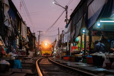 Maeklong Demiryolu Pazarı, Tayland, 5 Aralık 2025. Tren gün doğumunda yaklaşırken renkli kabinler raylara dizilir.