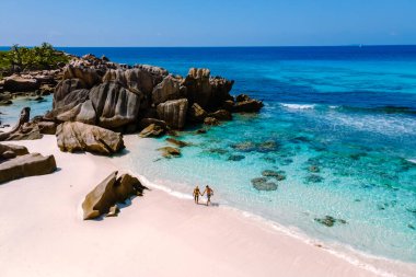 A couple strolls hand-in-hand along the soft, white sands of Anse Cocos beach on La Digue, Seychelles.
