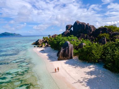 Two visitors stroll along the pristine shores of Anse Source d'Argent, surrounded by exotic rock formations and crystal-clear waters. A perfect setting for a relaxing holiday in La Digue, Seychelles