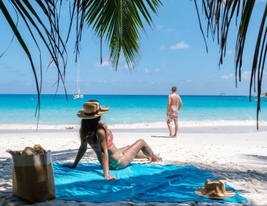 Palmiye ağacının altında dinlenen bir çift, Praslin, Seyşeller 'deki Anse Georgette' in çarpıcı turkuaz sularının ve yumuşak kumlarının tadını çıkarıyor. Bu huzurlu yer huzur arayan tatilciler için mükemmel bir yer..