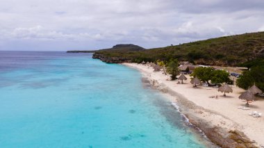 Berrak turkuaz sular, Cas Abao Beach Curacao 'nun kumlu sahillerinde güneşlenenlerin saman kulübelerinin altında dinlendiği yerde. Ziyaretçiler bu Karayip cennetinde yüzmeyi ve anıları yakalamayı severler..