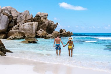 A joyful couple strolls hand in hand on the soft sands of Anse Cocos beach, surrounded by stunning granite rocks and crystal-clear waters. La Digue Seychelles