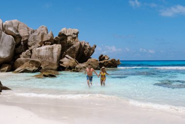 Seyşeller 'de parlak mavi bir gökyüzünün altında yüksek granit kayalar ve kristal berrak suyla çevrili Anse Cocos plajının yumuşak kumlarında el ele yürüyen çift. Rahatlamak için mükemmel bir kaçış..