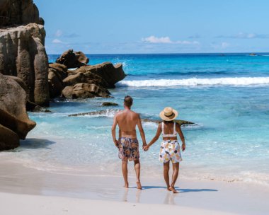 Two lovers stroll along the soft sands of Anse Cocos beach, surrounded by stunning rock formations and vibrant blue waters. A perfect vacation spot for relaxation and romance in Seychelles.