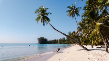 Ziyaretçiler Koh Kood, Tayland 'daki Khlong Hin Sahili' nin tadını çıkarırken, bir palmiye ağacının altında hafifçe sallanıyorlar. Saf kum ve berrak su güneşin altında rahatlamak ve eğlenmek için mükemmel bir ortam yaratır..