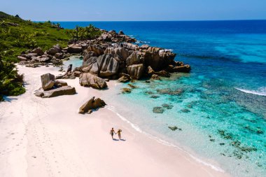 Anse Cocos sahilleri boyunca el ele yürüyen bir çift turkuvaz suları ve çarpıcı granit kayalar, La Digue, Seyşeller