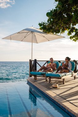 Willemstad, Curacao 'daki sakin Karayip sularında uzanan bir çift erkek ve kadın sonsuz havuz kenarında mükemmel bir tatil tatili geçiriyorlar..