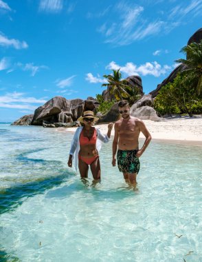 Kristal berrak sular ziyaretçileri Anse Source d 'Argent plajının büyüleyici güzelliğini keşfetmeye davet ediyor. Bir çift adam ve bir kadın La Digue, Seyşeller 'de tatildeler.