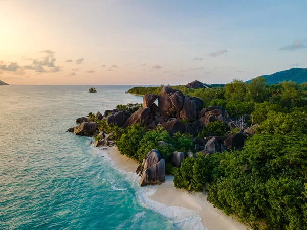 Güneş dramatik granit kayaların ardında batarken Anse Source d 'Argent kıyılarına doğru hafif hafif dalgalar süzülerek yemyeşil alanları aydınlatıyor. La Digue, Seyşeller