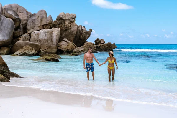 Couple walks hand in hand along the white sands of Anse Cocos Beach, surrounded by stunning granite rocks and crystal-clear waters. A perfect escape for lovers and travelers to La Digue Seychelles