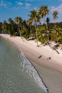 Ziyaretçiler Koh Kood, Tayland 'daki Khlong Hin Sahili' nin dingin güzelliğinin tadını çıkarıyorlar. Yumuşak dalgalar, mükemmel bir tatil gününde tropikal palmiyeler ılık esintide sallanırken kıyıda yavaşça süzülür..