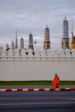 Bangkok, Tayland, 19 Kasım 2025, Wat Phra Kaew yakınlarındaki sokakta yürüyen bir keşiş, bu ikonik tapınağın karmaşık mimarisini ve huzurlu çevresini gözler önüne seriyor..