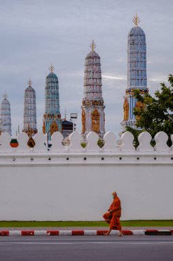 Bangkok, Tayland, 19 Kasım 2025. Turuncu cüppeli bir keşiş görkemli Wat Phra Kaew 'in yanından geçerken sakin bir arkaplan karşısında çarpıcı bir mimari sergiliyor..