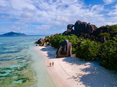 İki kişi verimli yeşillikler ve parlak mavi bir gökyüzü altında çarpan granit kayalarla çevrili Anse Kaynağı d 'Argent' ın el değmemiş kumları boyunca rahatça yürür. La Digue, Seyşeller