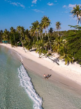 Koh Kood, Tayland 'daki Khlong Hin Sahili' nin el değmemiş beyaz kumları boyunca bir çift yürüyüş. Berrak suların ve parlak mavi gökyüzünün altında sallanan palmiyelerin tadını çıkar. Huzurlu bir kaçış için mükemmel..