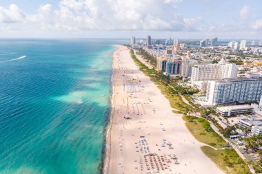 Parlak gökyüzü ve turkuaz sular, güneşlenenlerin kumlu kıyılarda dinlendiği Miami Sahili 'nin çevresini sarar. Renkli şemsiyeler kıyı şeridini dolduruyor, canlı bir tatil ortamı yaratıyor..