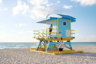 Ziyaretçiler, Miami Sahili 'ndeki ikonik cankurtaran kulesinde sıcak güneşin altında dinleniyor. Bu popüler tatil beldesinin kıyı manzarasının ve hareketli atmosferinin tadını çıkarıyorlar..