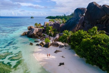 İki gezgin, Anse Kaynak d 'Argent sahilinin el değmemiş beyaz kumları boyunca, dramatik granit kayalar ve canlı palmiyelerle çevrili bir şekilde geziniyor. La Digue, Seyşeller