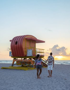 Miami Plajı 'nda güneş batarken kumlu sahil boyunca birkaç yürüyüş, gökyüzünün canlı renklerinin ve ünlü cankurtaran kulesinin tadını çıkarıyor. Mükemmel bir tatil anı..