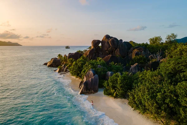 La Digue, Seyşeller 'deki Anse Source d' Argent 'ta sakin sahil sahnesi, gün batımında sahilde yürüyen adam, insansız hava aracı manzarası.