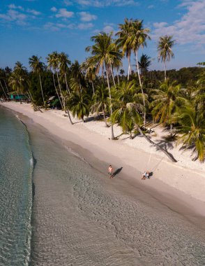 Koh Kood, Tayland 'daki Khlong Hin Sahili' nin yumuşak kumlarında rahatlayın. Bu tropikal cennetin huzur ve güzelliğinin tadını çıkararak, sahil boyunca yürüyen ziyaretçiler gibi palmiye ağaçları yavaşça sallanıyor..