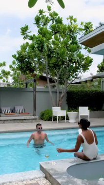 Havuz kenarında sakin bir öğleden sonranın tadını çıkar, lüks bir villada yemyeşil bir yer. Soğuk suda gevşeyen, içkilerini yudumlayan ve huzurlu atmosferi kucaklayan bir çift..