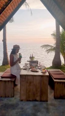 Koh Mak Tayland 'da sakin bir sahilde doğa tarafından çevrili lezzetli bir yemeğin tadını çıkarıyorum. Çarpıcı günbatımı masanın üzerinde sıcak bir parıltı yayar ve mükemmel bir tatil atmosferi yaratır..