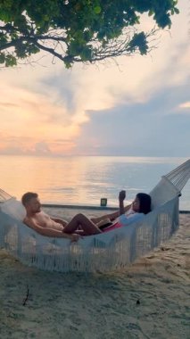 Hua Hin, Tayland 'ın kumlu sahillerinde hamakta uzanan iki insanın mutlu sahnesinin tadını çıkarın. Canlı günbatımı, unutulmaz anılar yaratmak için mükemmel romantik bir ortam yaratır..