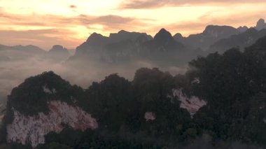 Güneş doğarken Khao Sok, Tayland 'ın göz kamaştırıcı güzelliğine tanık olun. Sis, canlı yeşillik ve görkemli zirvelerin üzerine çöker. Doğaya mükemmel bir kaçış. Gezgin aşıklar için kucaklaşma..