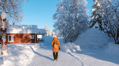 Bir gezgin, Akaslompolo Köyü 'nde karla kaplı bir patika boyunca yürüyor. Etrafı buz gibi ağaçlar ve rahat ahşap kulübelerle çevrili. Laponya Finlandiya 'da, bir kadın ahşap bir kulübeye giden karlı bir yolda yürür.