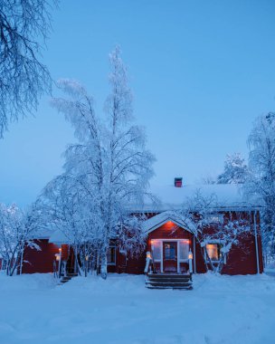Alacakaranlıkta Laponya, Akaslompolo 'da sakin, karlı bir arazide yakalanan büyüleyici kırmızı kulübe. Karla kaplı görkemli ağaçlar kış maceraları için büyülü bir atmosfer yaratır..